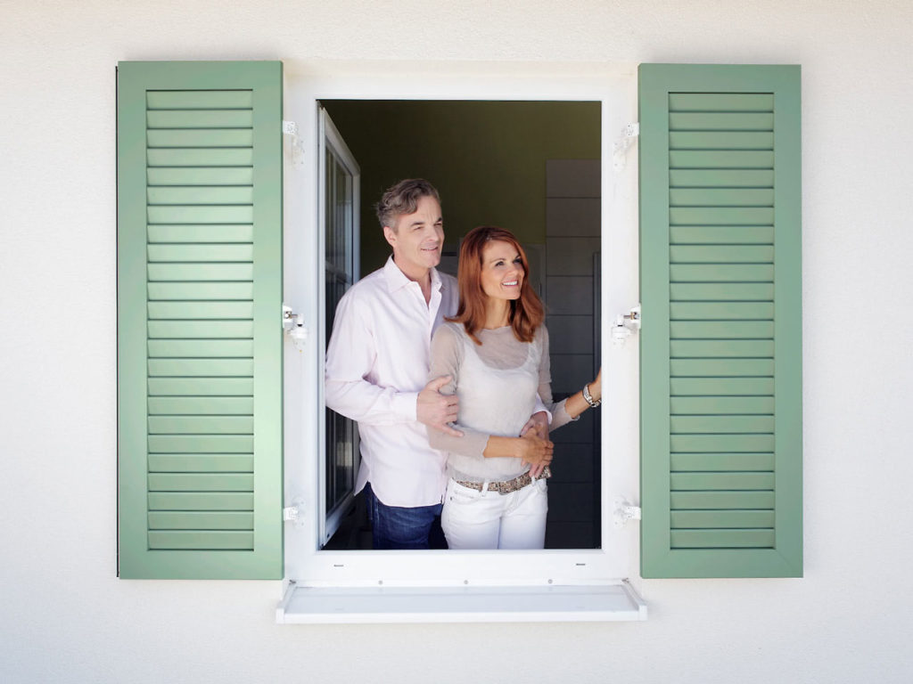 Frau und Mann stehen romantisch an einem Fenster mit hellgrünen Klappfensterläden
