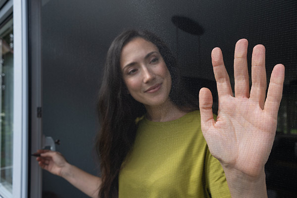 Frau berührt Fliegengitter mit ihrer Hand